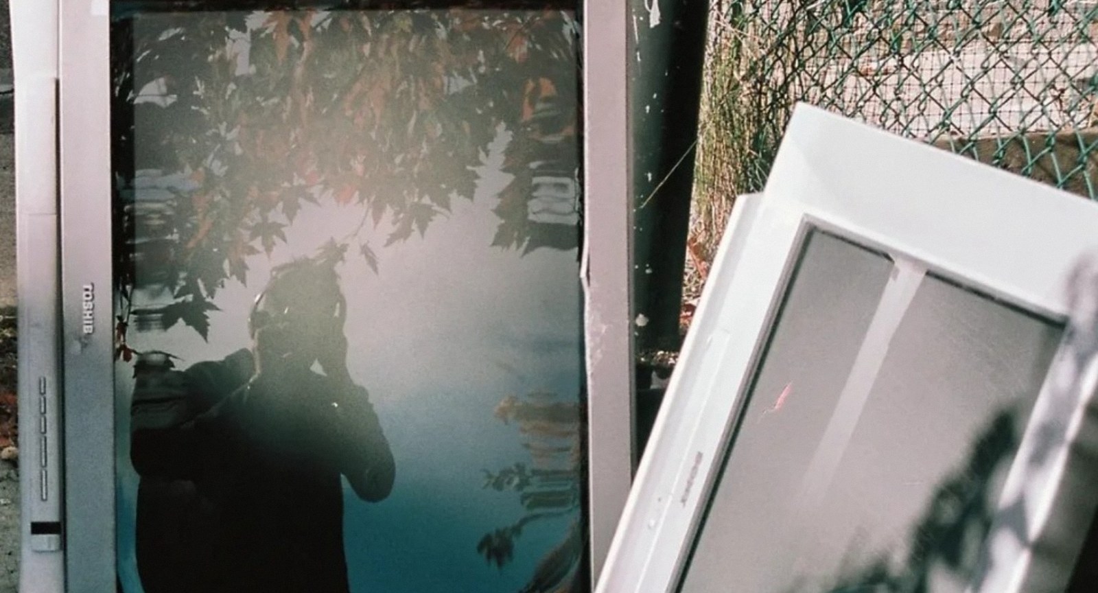 Discarded television and picture frames outdoors, reflecting trees and the photographer.